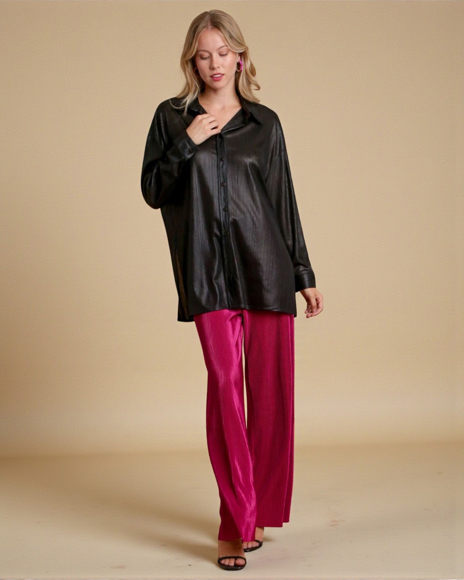 Woman wearing a black satin shirt and pink pants against a beige background