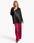 A woman modeling a black faux-leather button-up shirt and bright magenta wide-leg trousers against a clean white studio background.