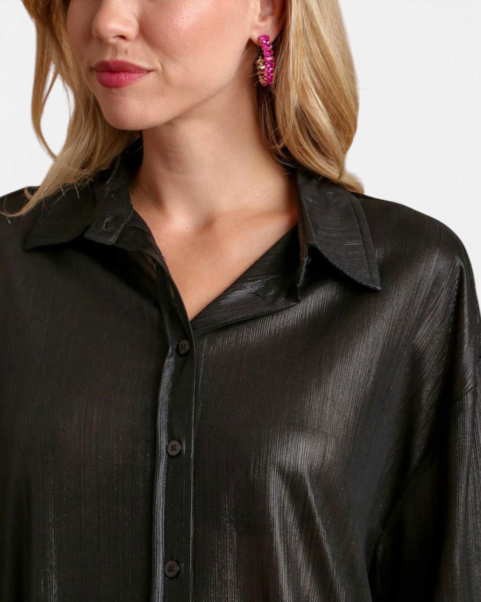 Close-up of a woman wearing a black textured button-up shirt with a collar, paired with a bright pink beaded earring, against a light gray background.