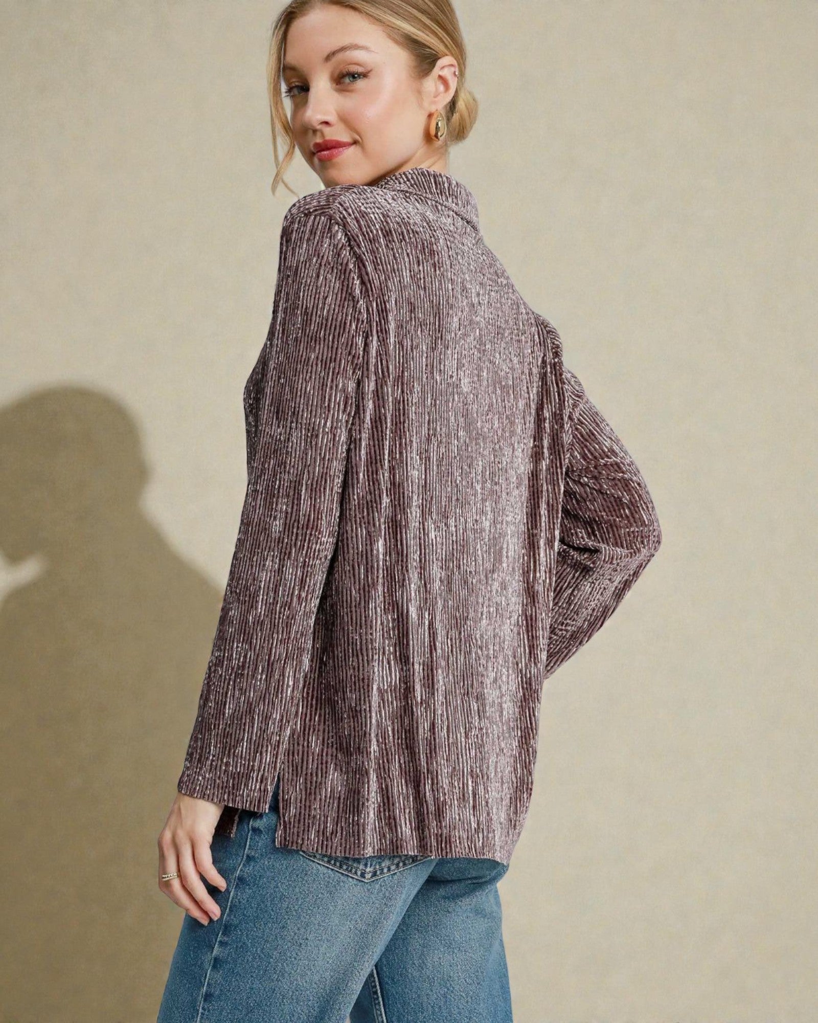 Woman wearing a textured brown jacket and blue jeans against a beige background