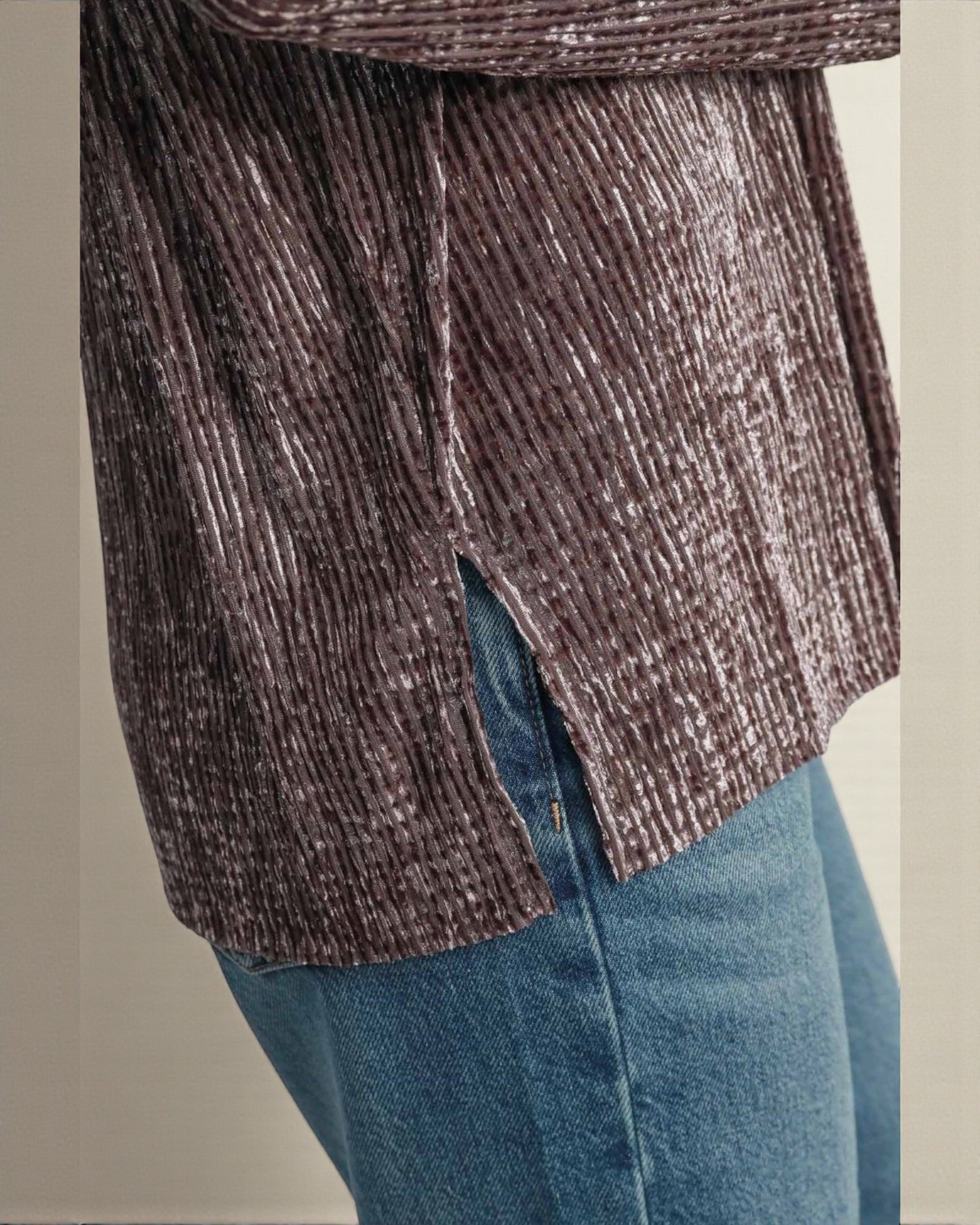 Close-up of a textured brown sweater and blue jeans against a neutral background