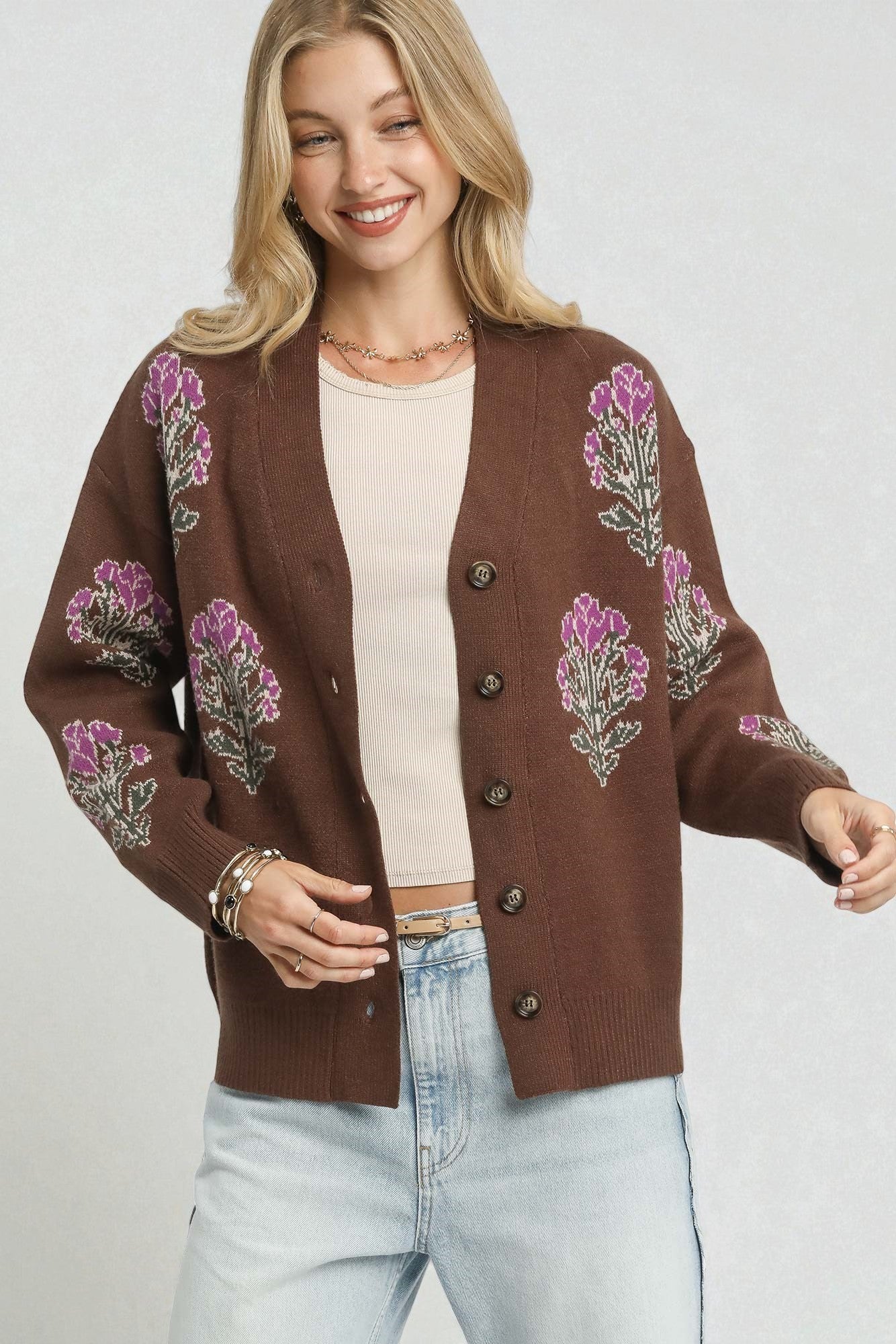 Woman wearing a brown cardigan with floral embroidery on a plain background