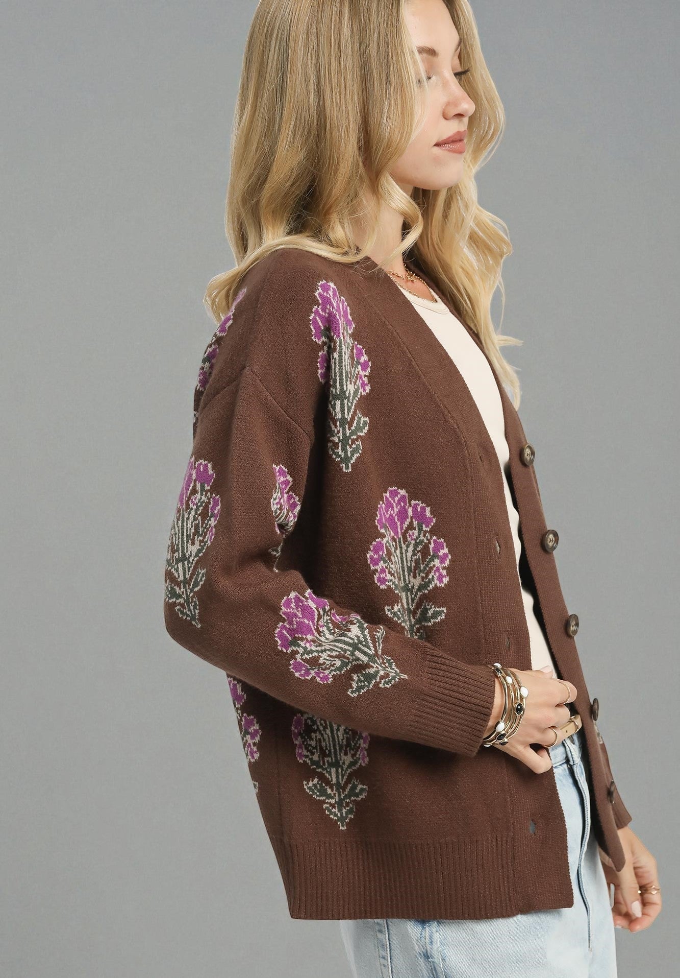 Woman wearing a brown cardigan with floral patterns on a gray background