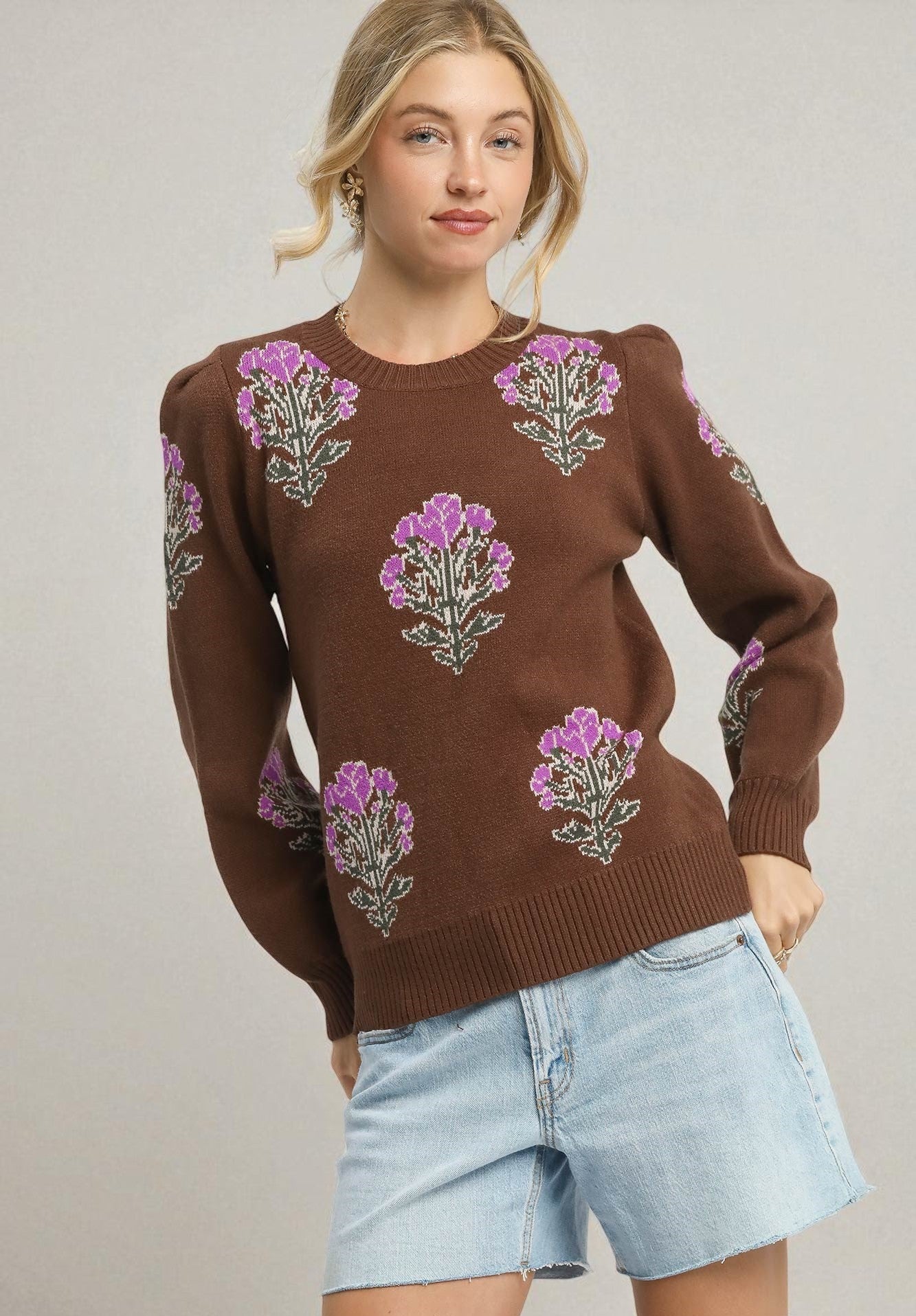 Woman wearing a brown sweater with floral patterns on a plain background