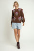 Woman wearing a brown sweater with floral patterns, light blue shorts, and brown boots on a white background