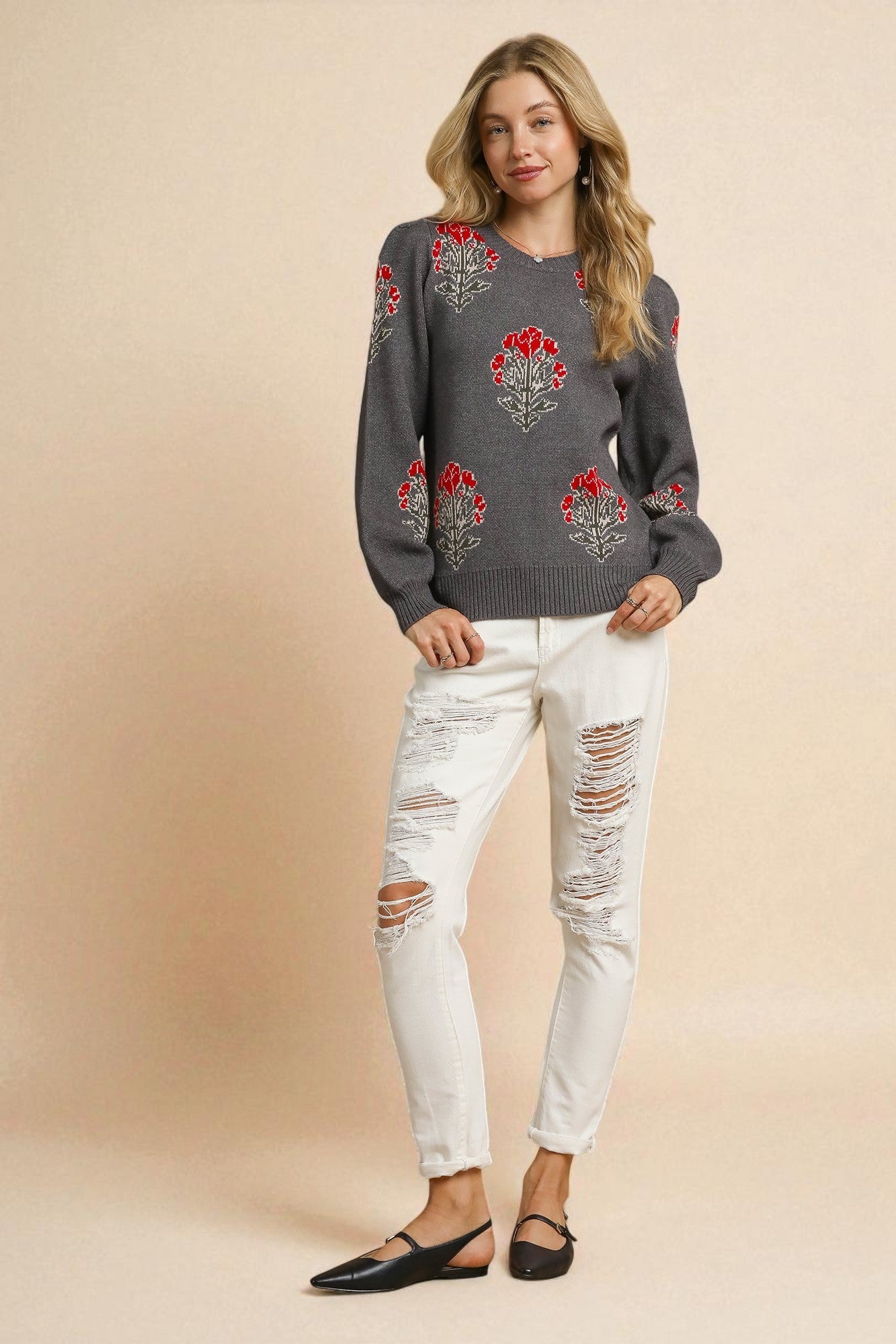 Woman wearing a gray sweater with floral patterns and white distressed jeans on a beige background