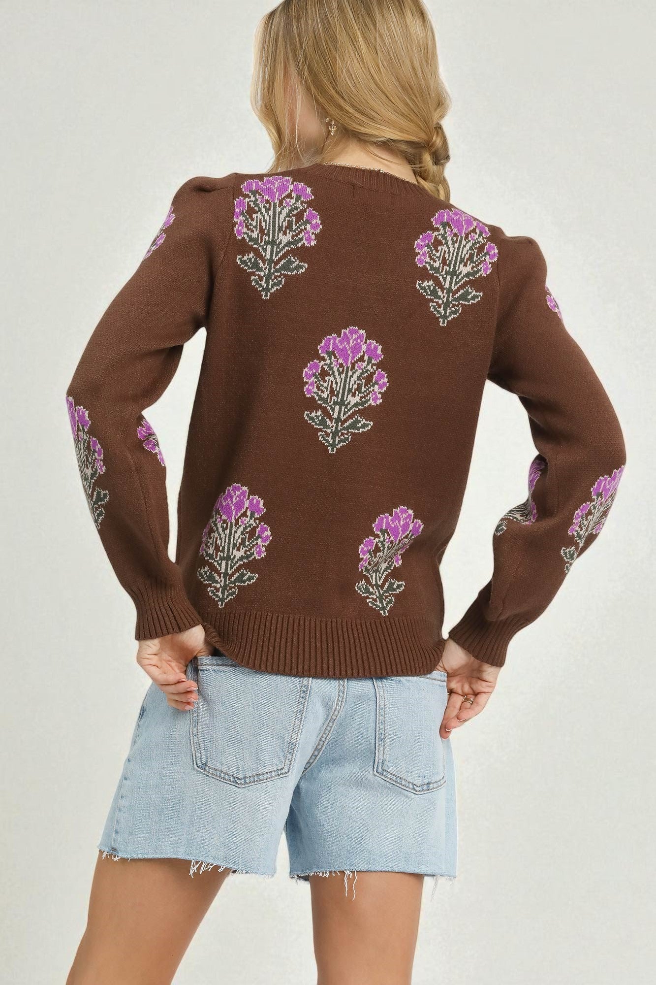 Brown sweater with floral patterns worn by a person on a plain background