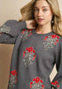Woman wearing a gray sweater with red floral patterns on a beige background
