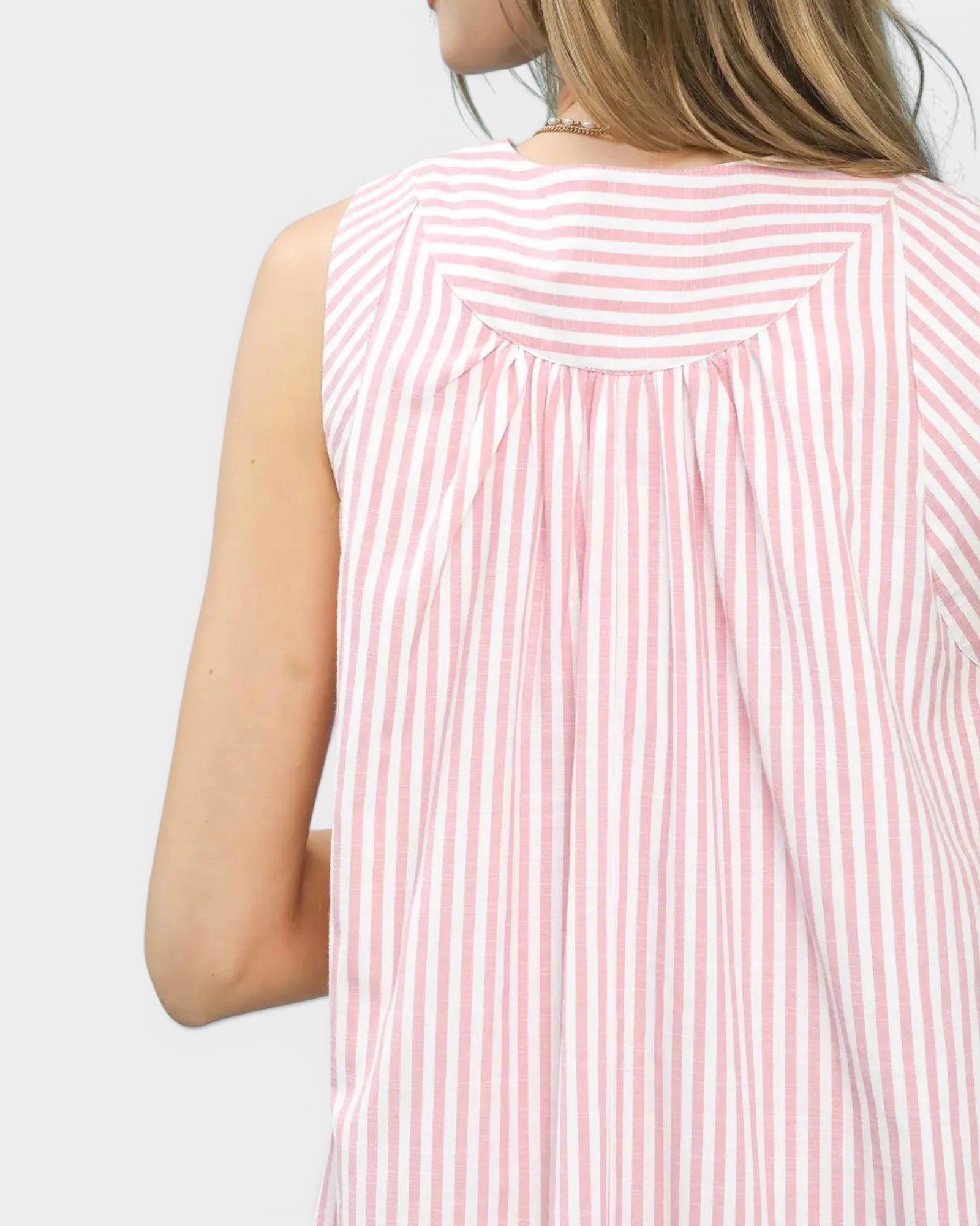 Pink and white striped sleeveless top worn by a person on a light gray background