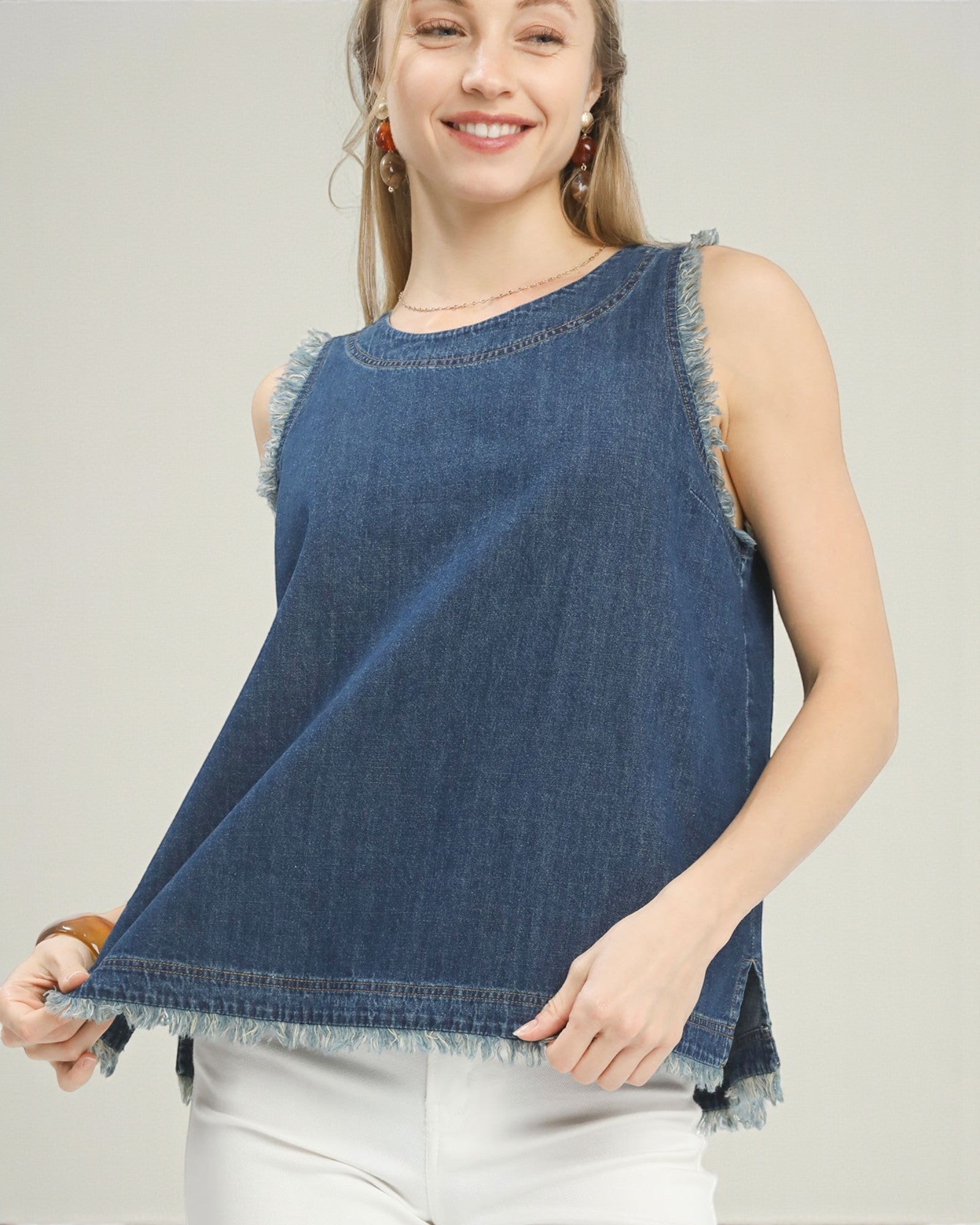 Woman wearing a blue denim sleeveless top with fringe details on a plain background