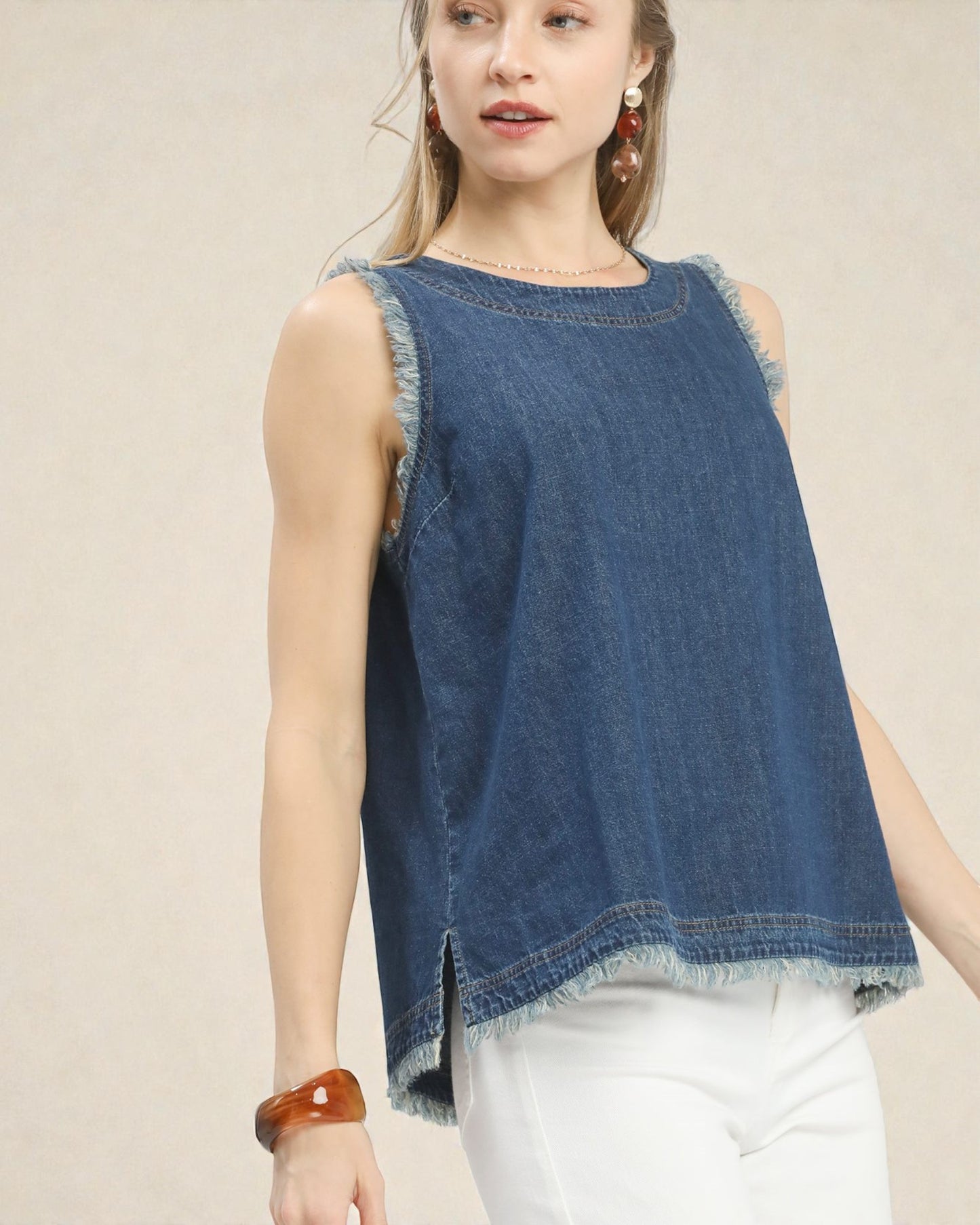 Woman wearing a blue denim sleeveless top against a beige background