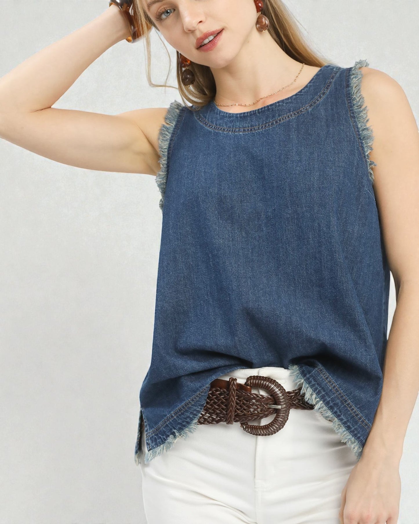 Woman wearing a denim sleeveless top with a belt on a plain background
