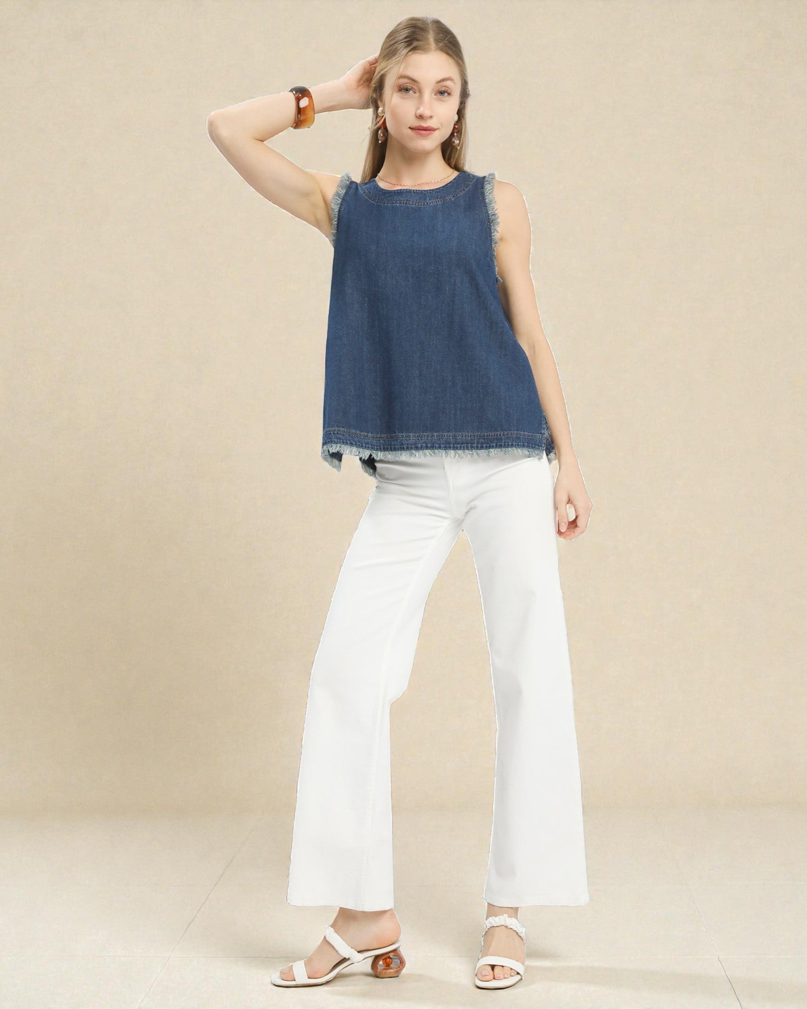 Woman wearing a blue denim top and white pants against a beige background