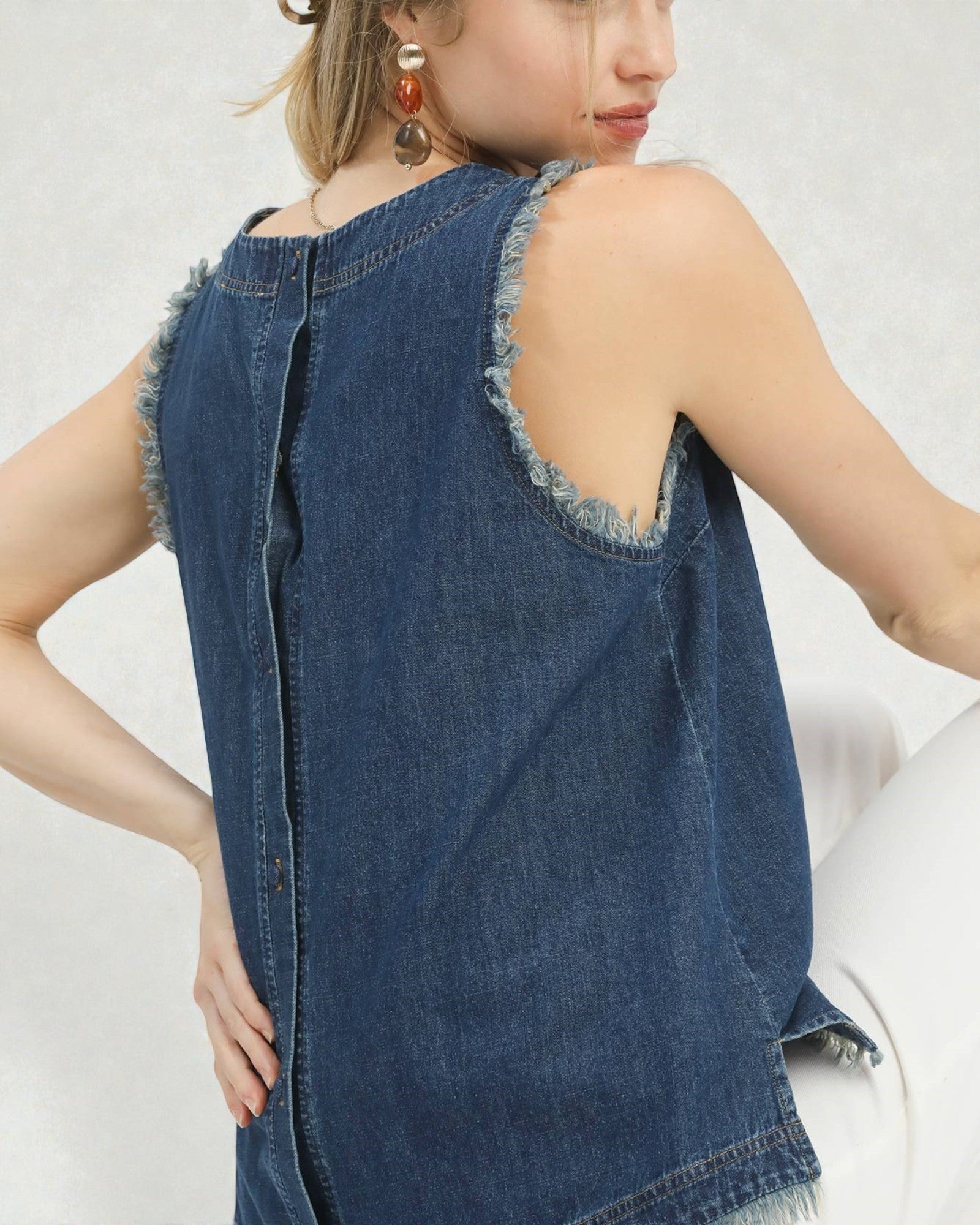 Woman wearing a blue denim sleeveless top with frayed edges on a white background