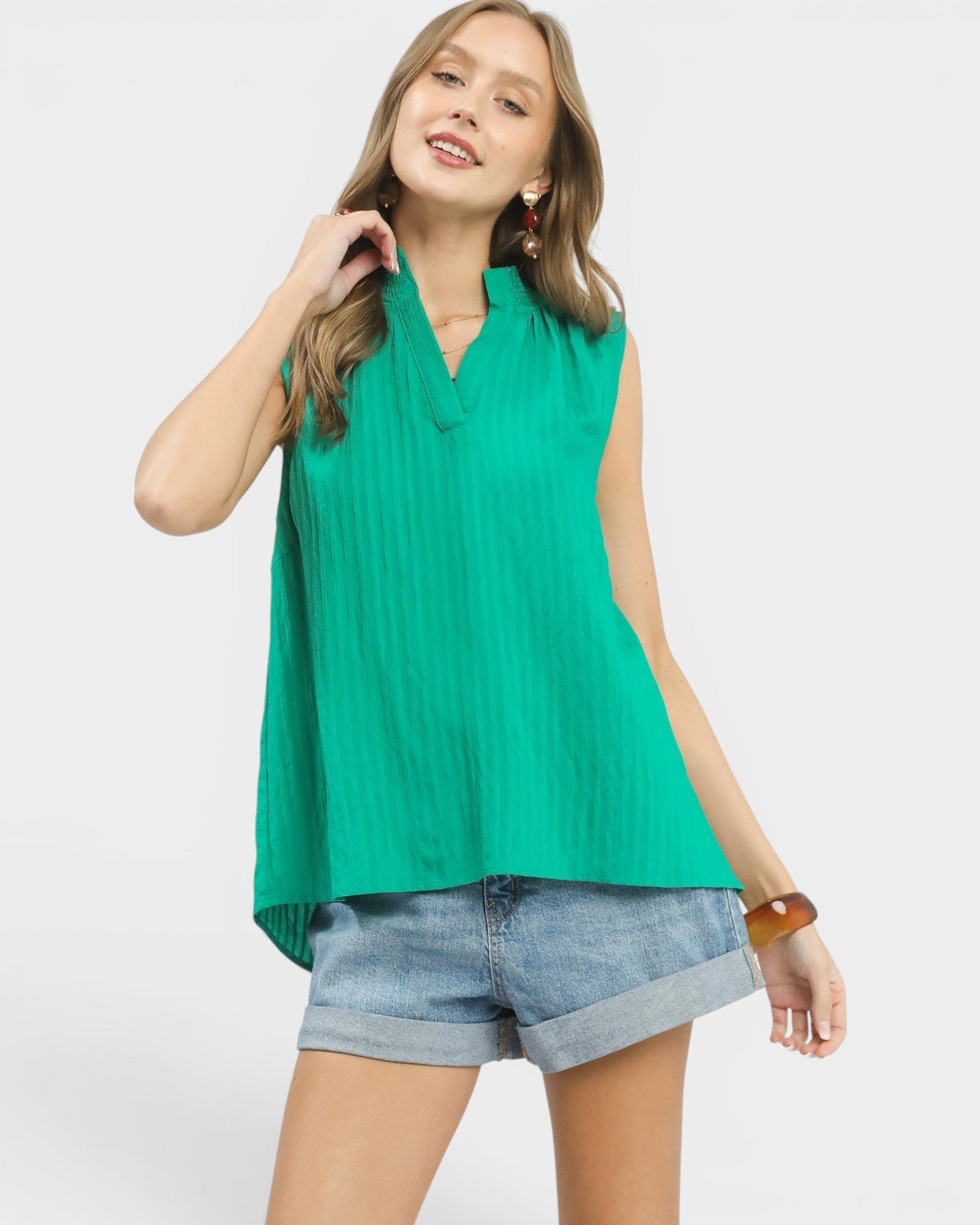 Woman wearing a green sleeveless top and denim shorts on a white background