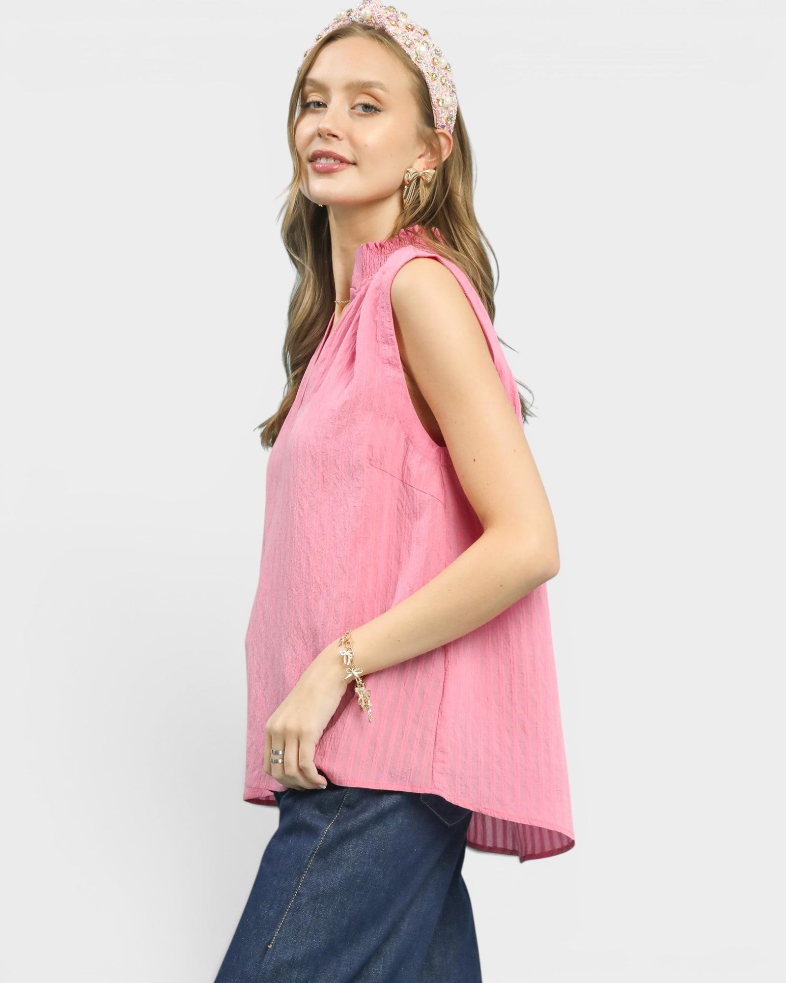 Woman wearing a pink sleeveless top and blue jeans on a white background