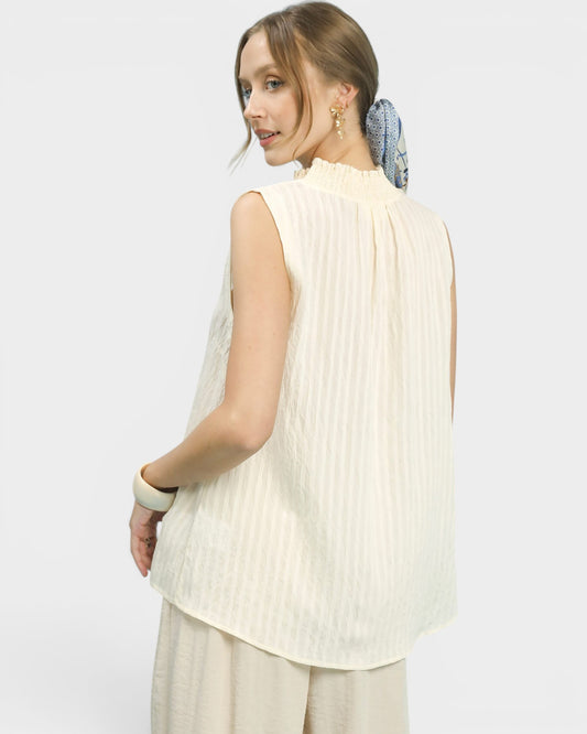 Woman wearing a cream-colored sleeveless top with pleated details on a white background