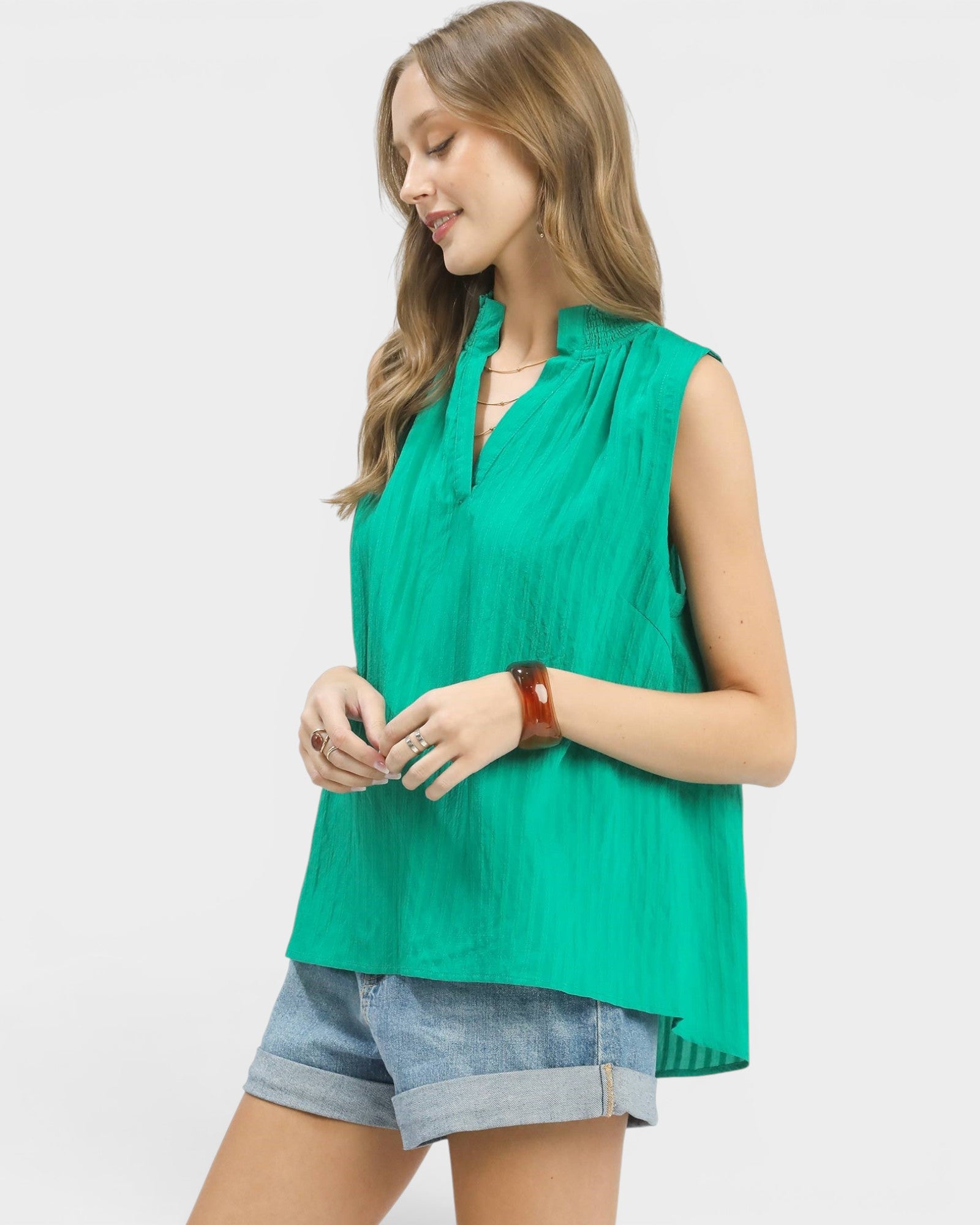 Woman wearing a green sleeveless top and denim shorts on a white background