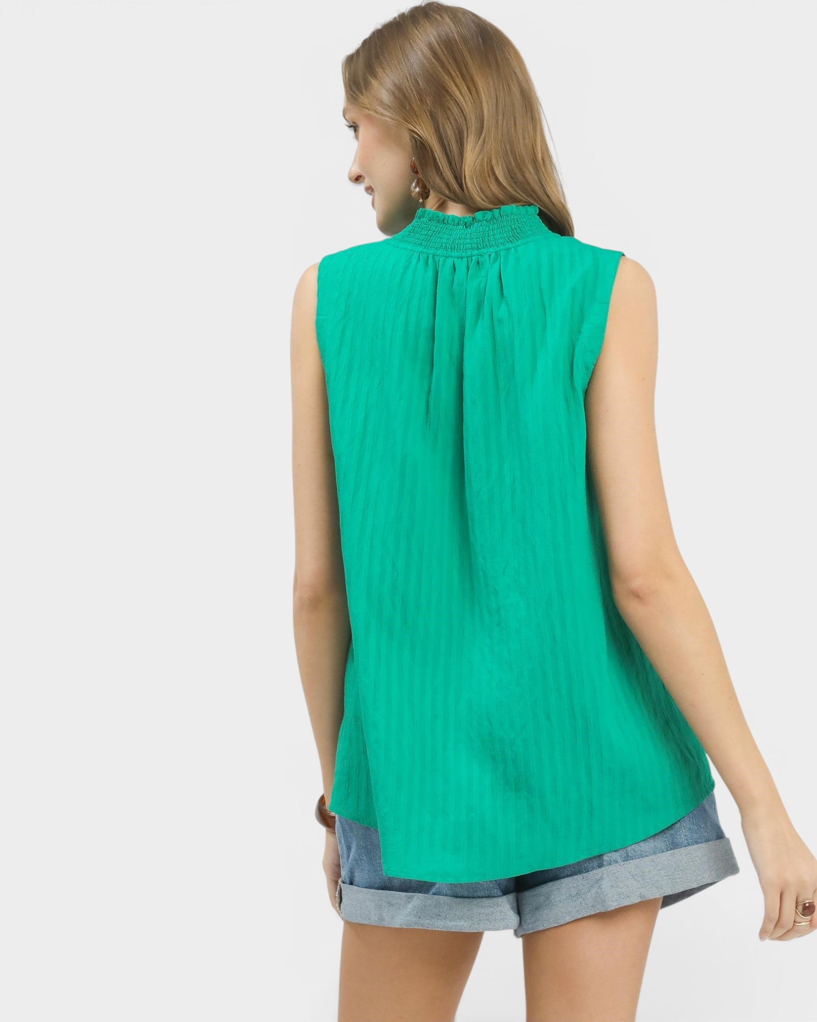 Woman wearing a green sleeveless top and gray shorts on a white background