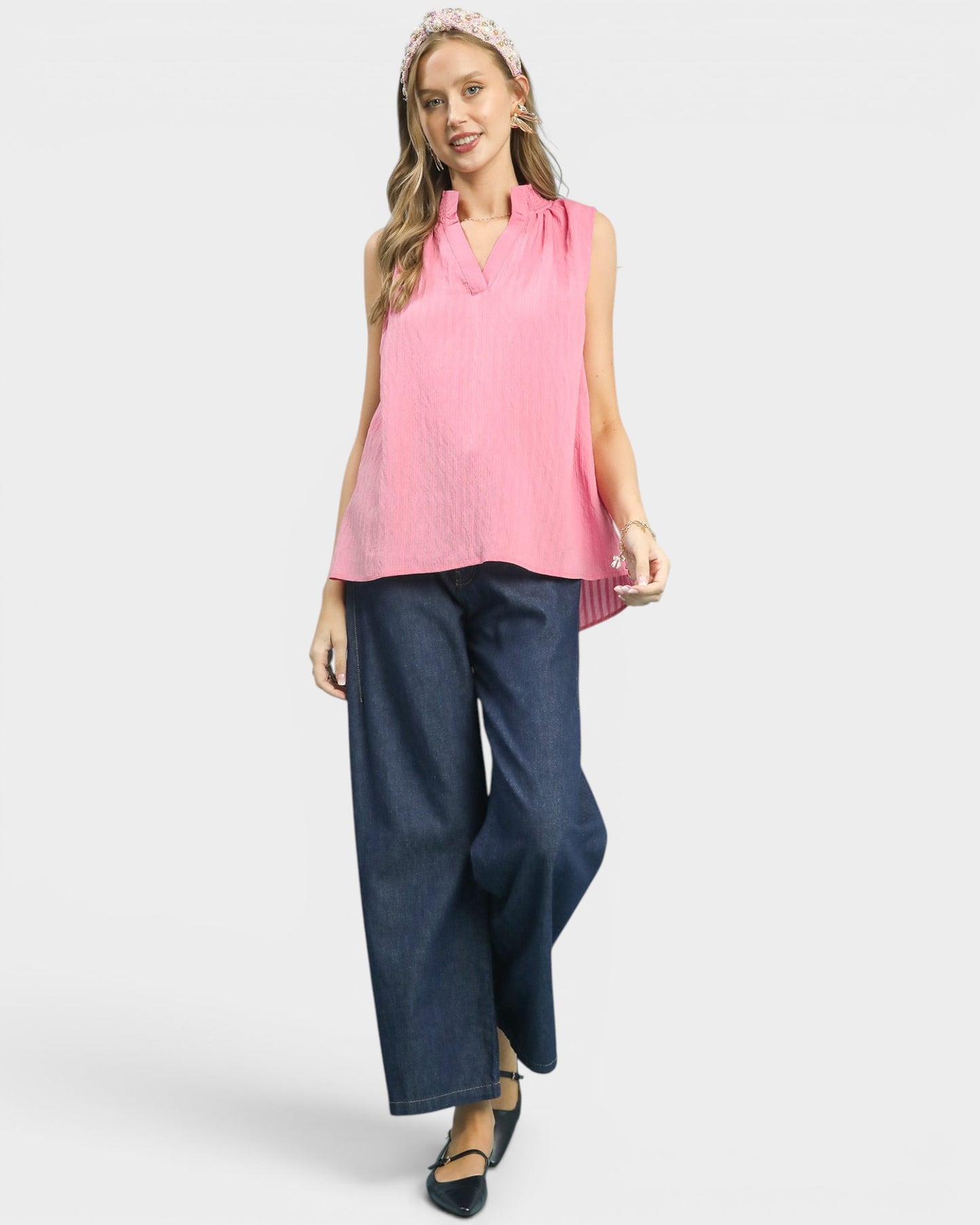 Woman wearing a pink sleeveless top and blue wide-leg pants on a white background