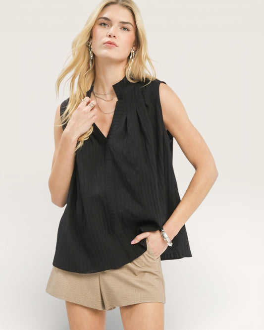 Woman wearing a black sleeveless top and beige shorts on a plain background