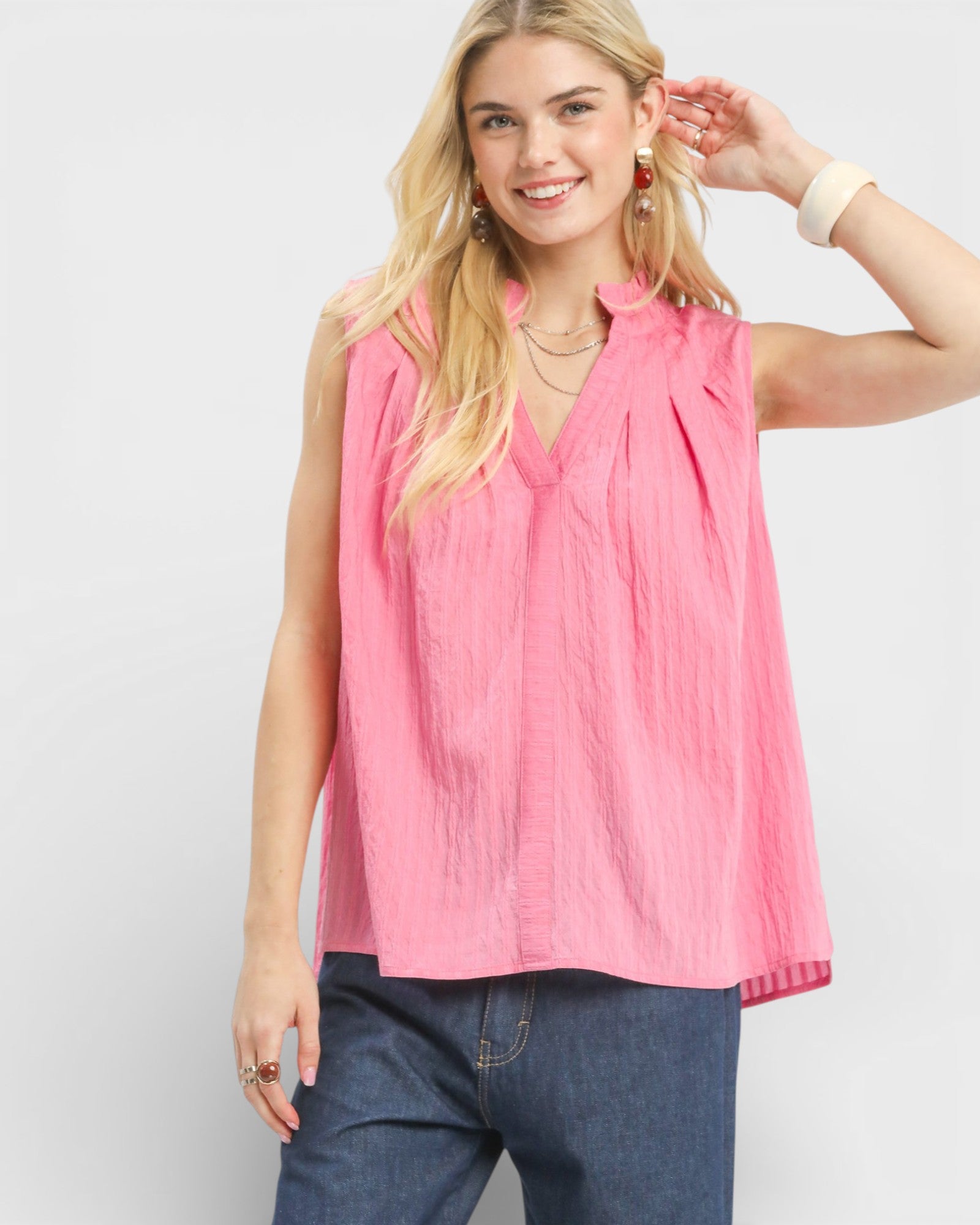 Woman wearing a pink sleeveless top and blue jeans on a white background
