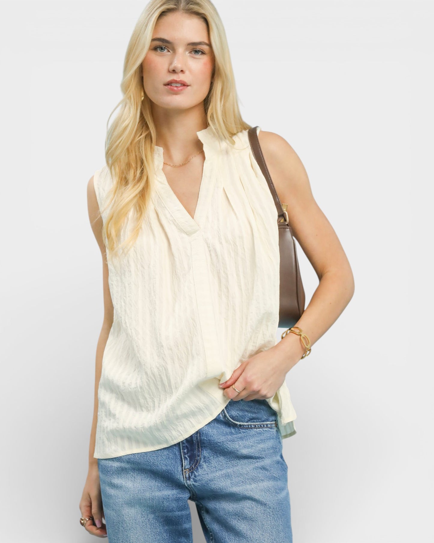 Woman wearing a light-colored sleeveless top and blue jeans against a white background