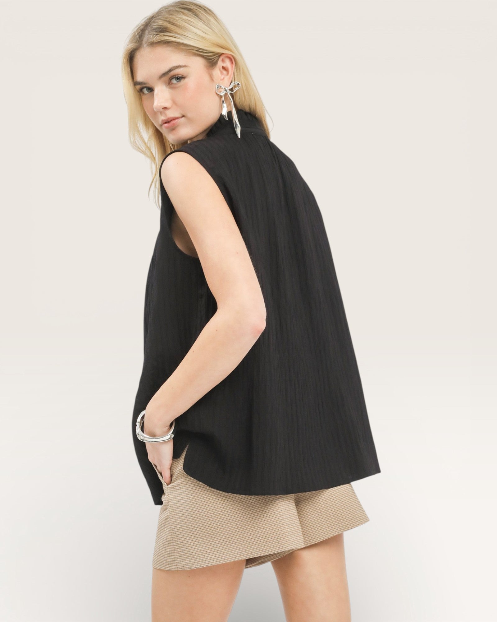 Woman wearing a black sleeveless top and beige shorts on a plain background