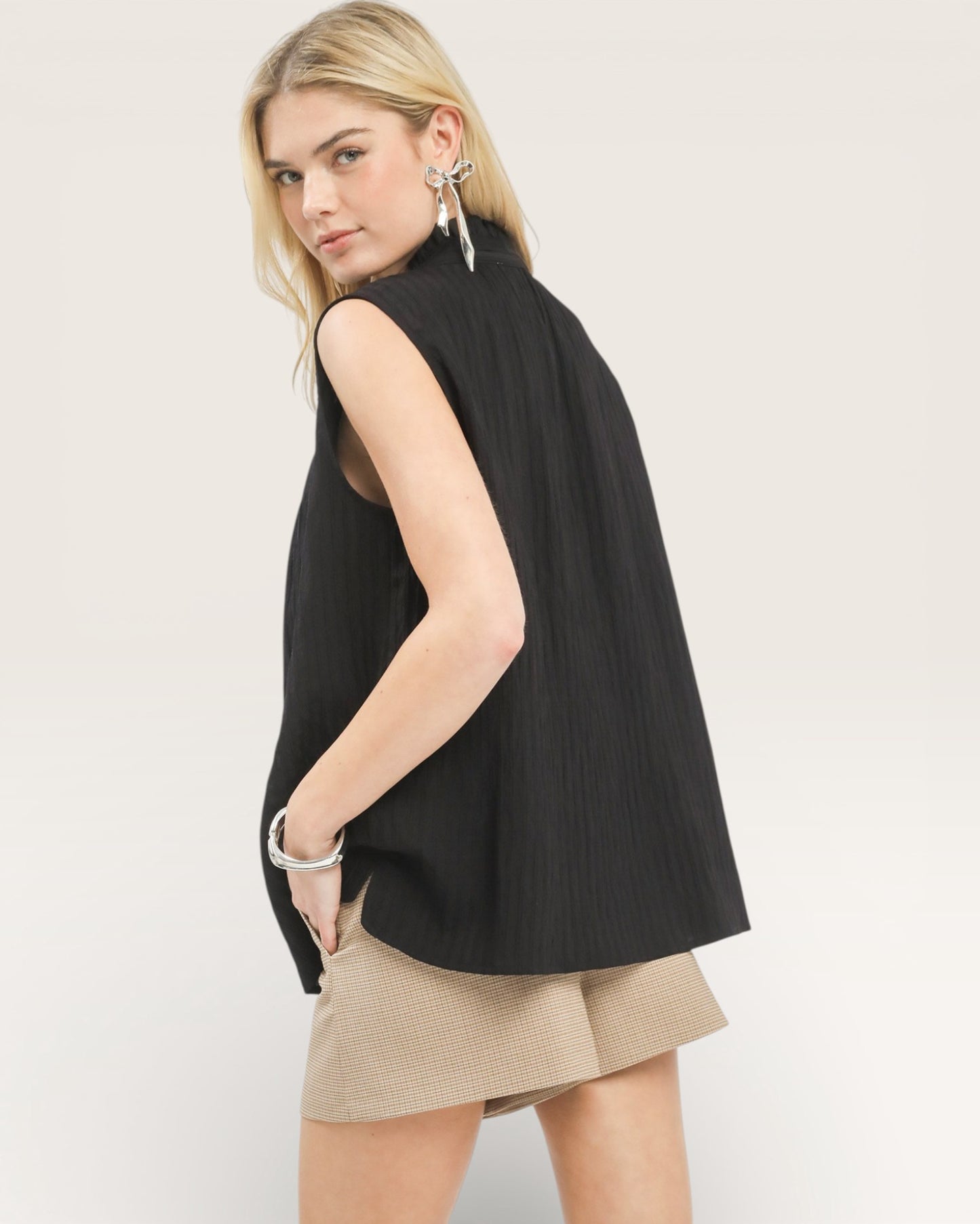 Woman wearing a black sleeveless top and beige shorts on a plain background