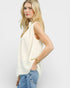 Woman wearing a sleeveless cream top and blue jeans on a plain background