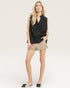 Woman wearing a black sleeveless top and beige shorts on a white background