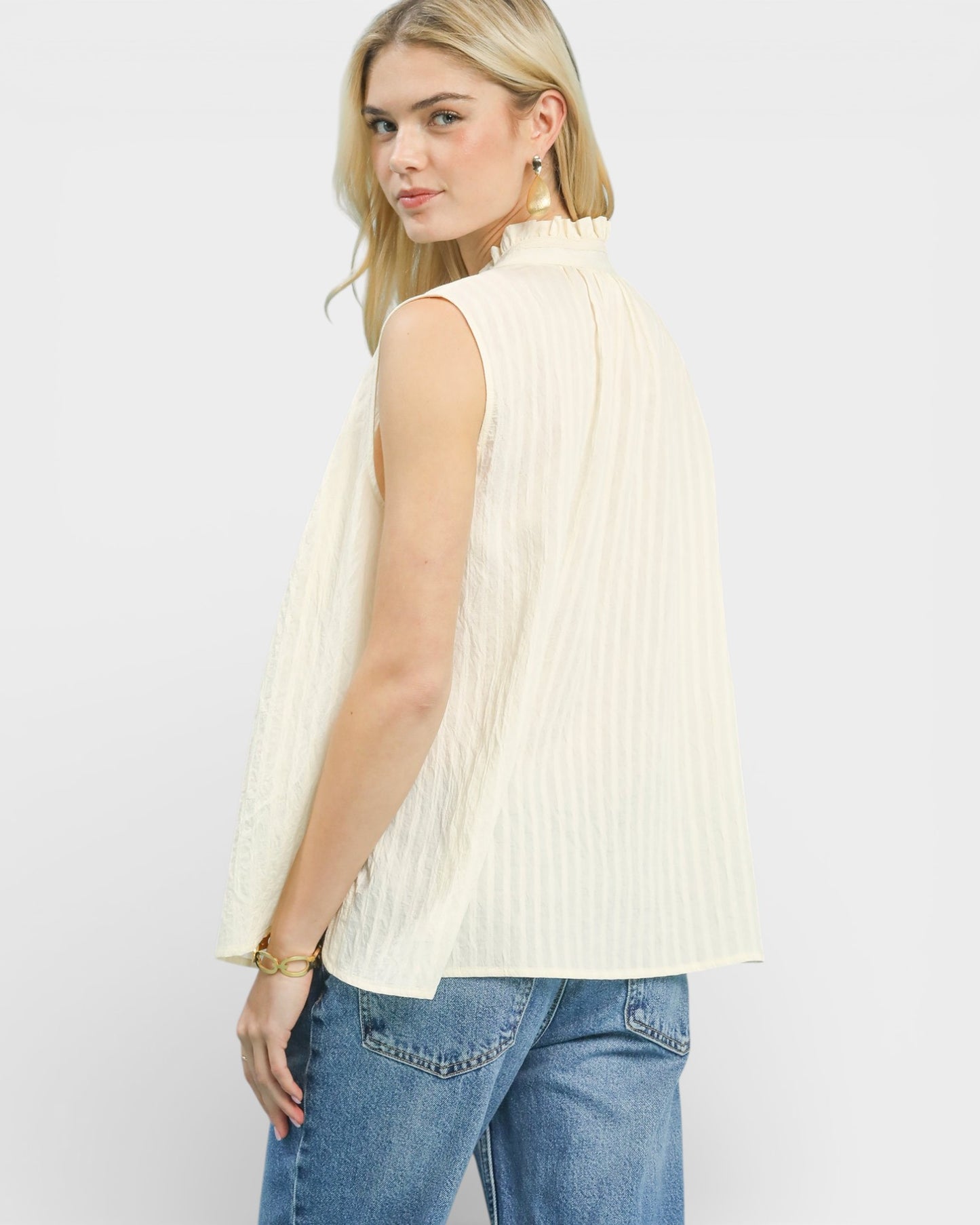 Woman wearing a sleeveless cream ribbed top and blue jeans on a white background