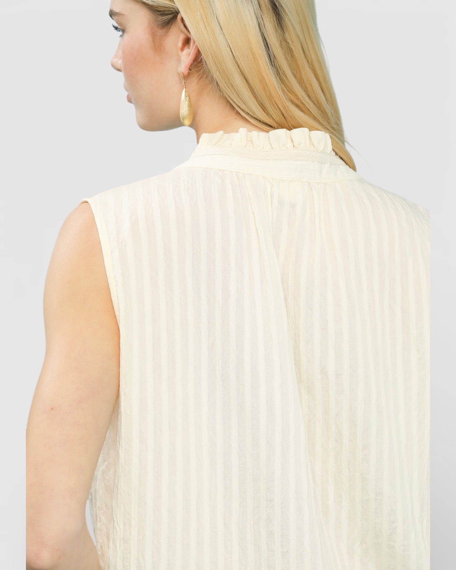 Woman wearing a light-colored sleeveless ribbed top against a plain background