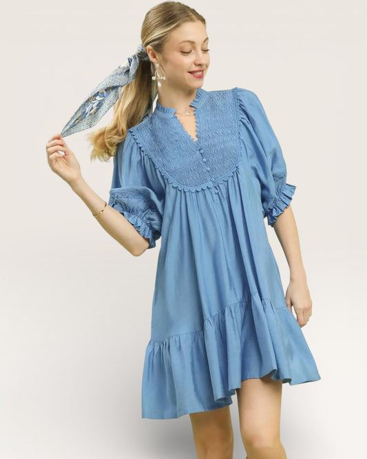 Woman wearing a blue dress holding a matching scarf against a plain background