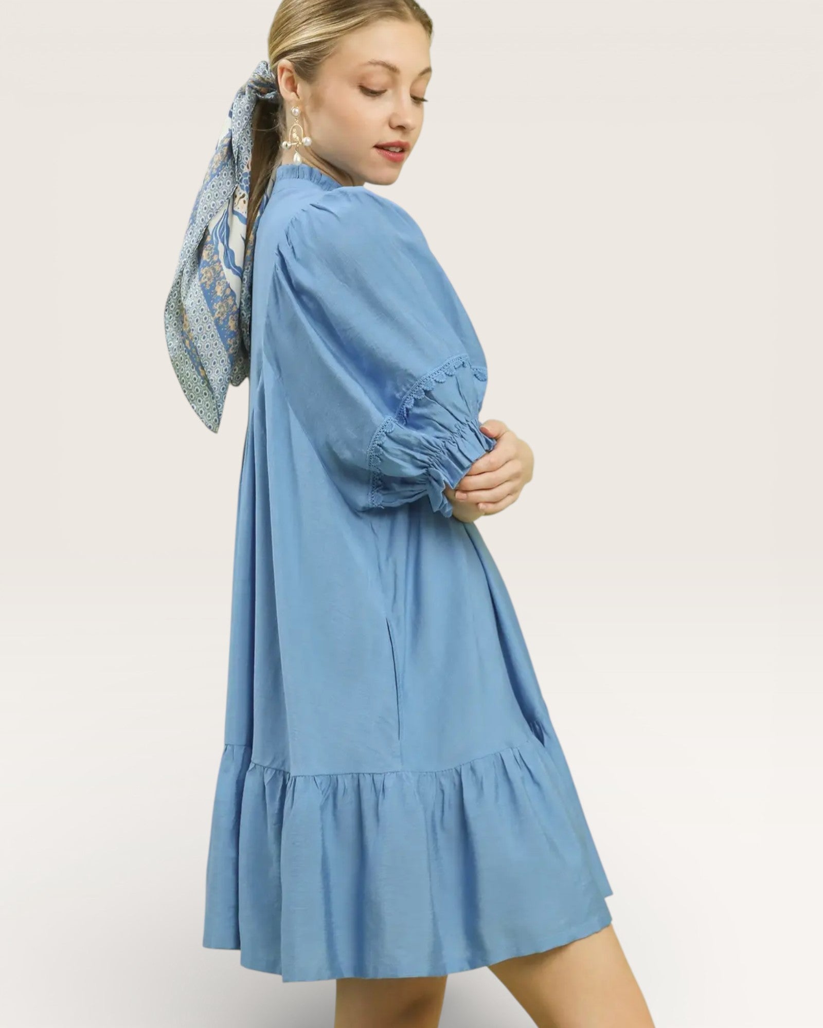 Woman wearing a blue dress with long sleeves and a scarf on her head against a white background