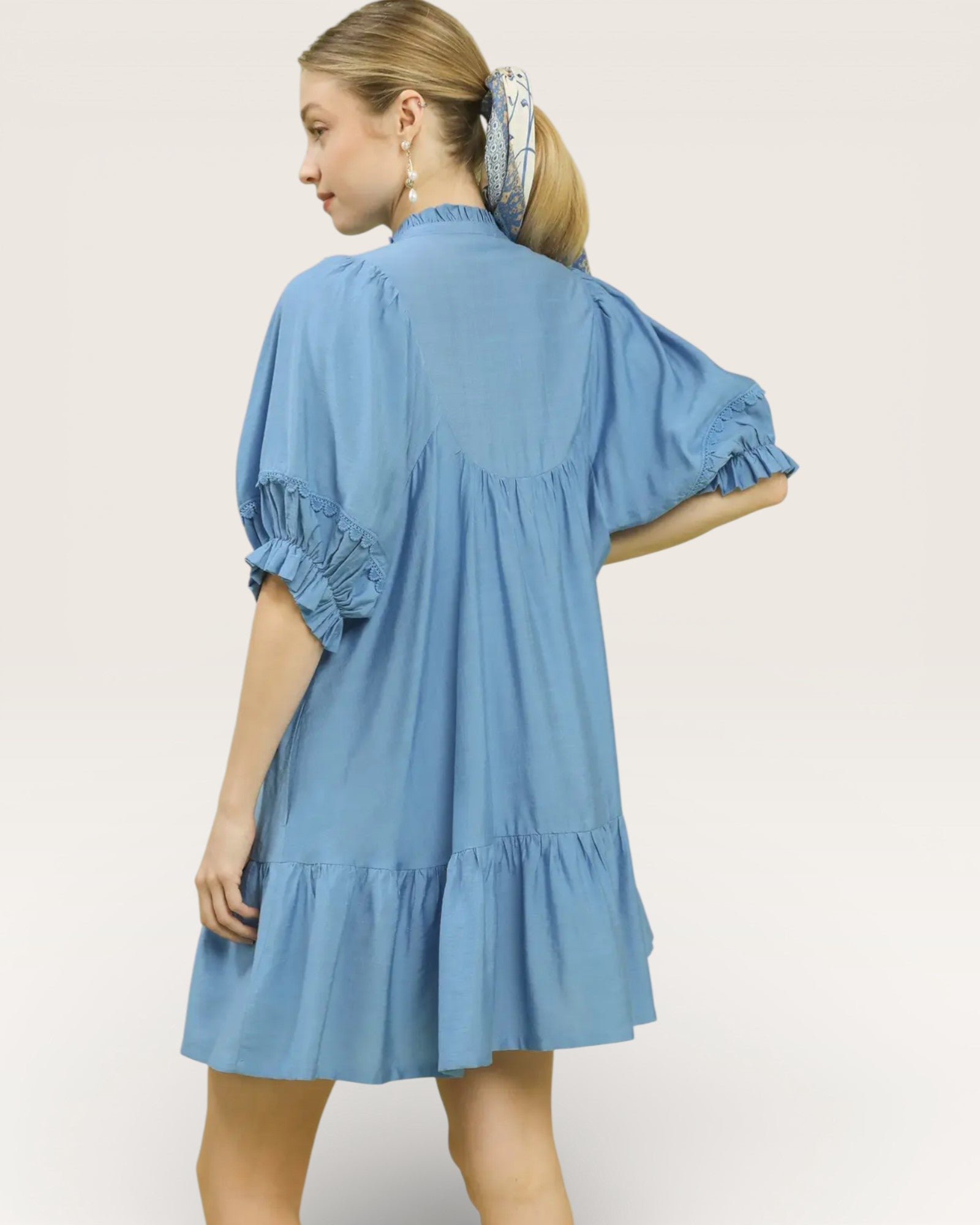 Woman wearing a blue dress with ruffled sleeves and hem on a light gray background