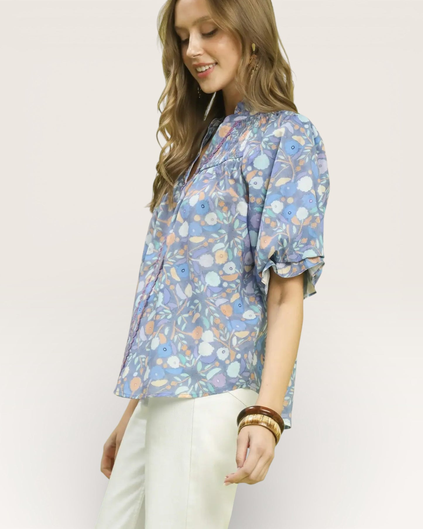 Woman wearing a blue floral blouse with white pants on a plain background