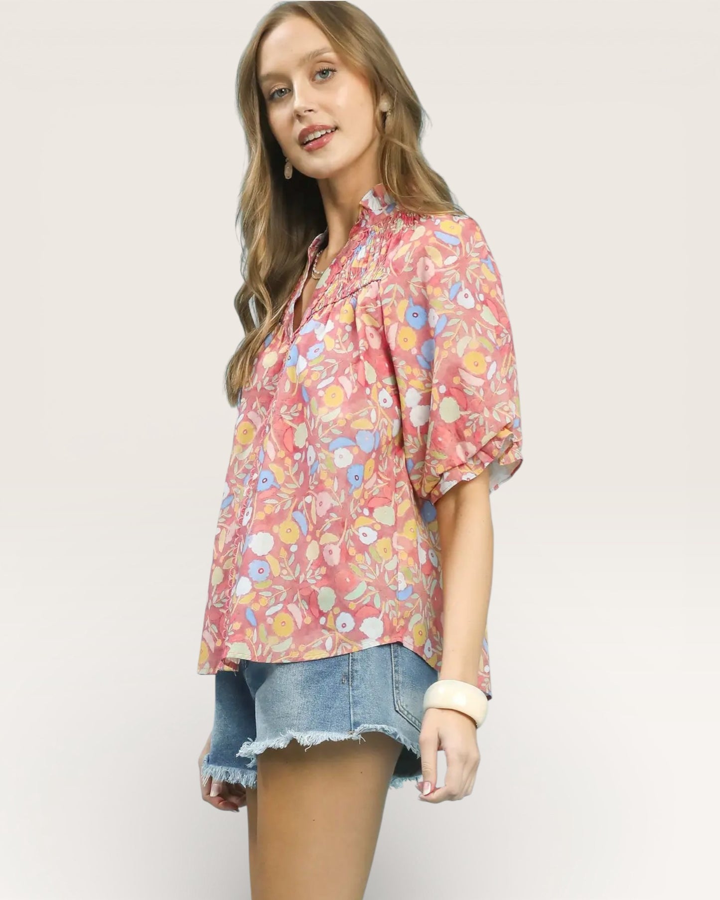 Woman wearing a floral blouse and denim shorts on a plain background