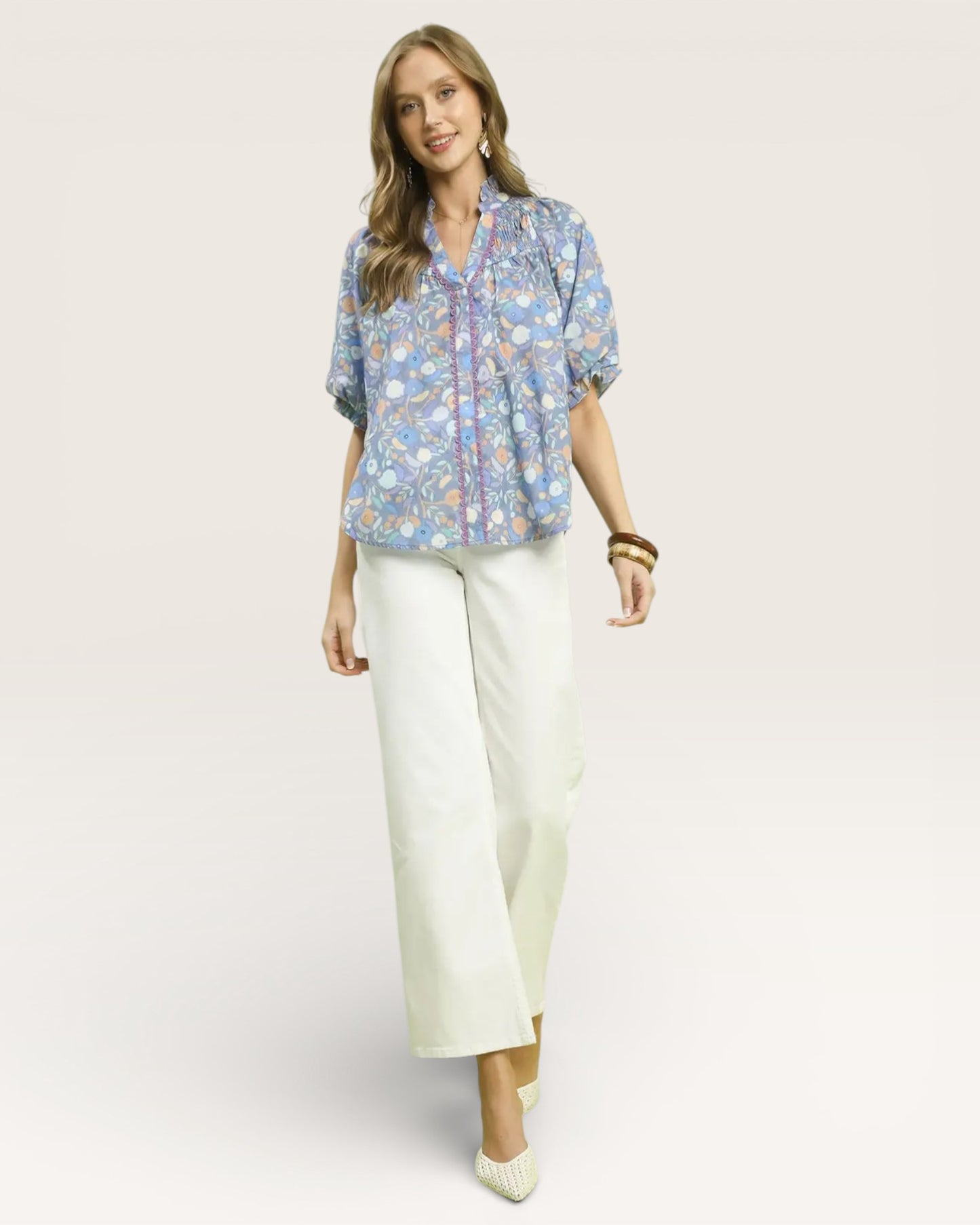 Woman wearing a floral blouse and white pants on a light pink background