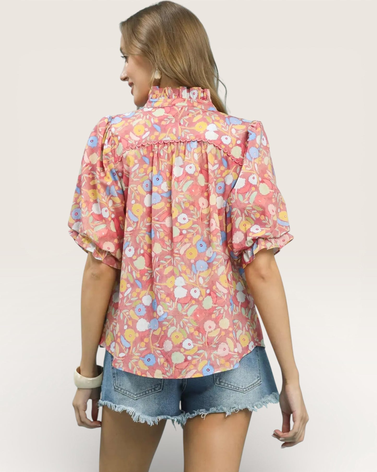 Woman wearing a floral blouse and denim shorts on a plain background