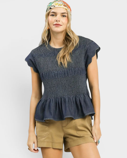 Woman wearing a dark blue textured top and beige shorts on a white background