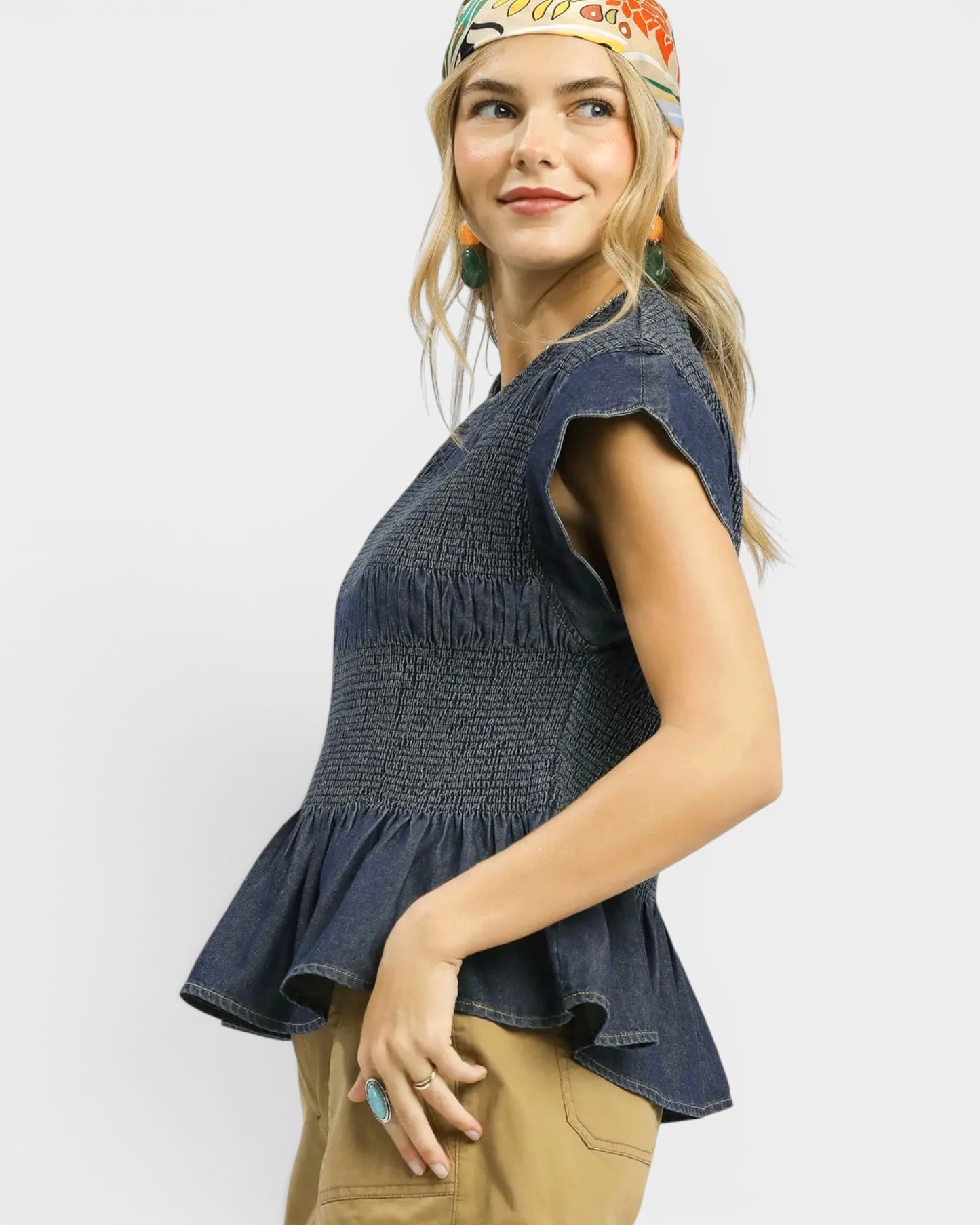 Woman wearing a denim peplum top and beige pants on a white background