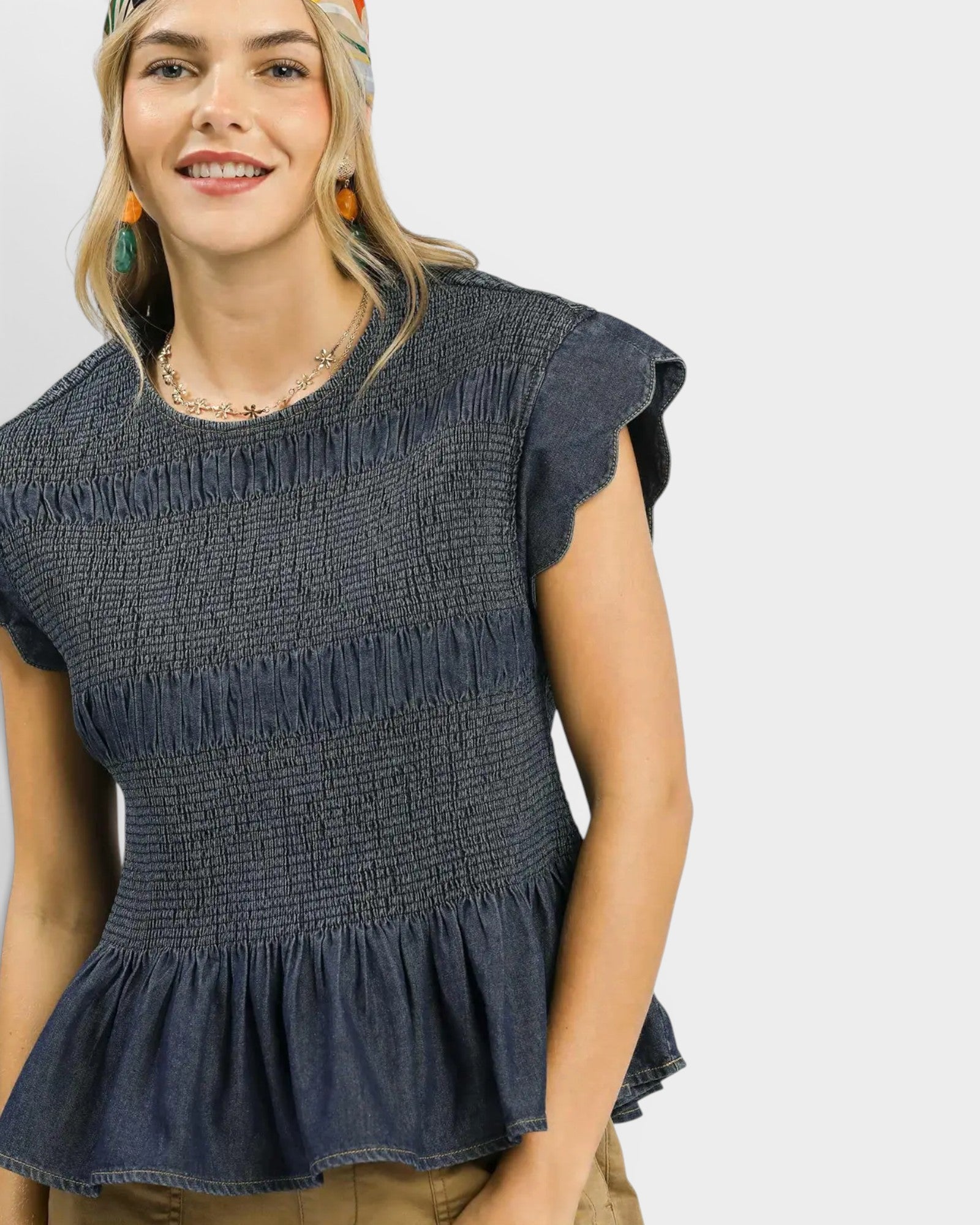 Woman wearing a dark denim top with ruffled details on a plain background