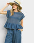 Woman wearing a blue top and pants with a straw hat on a light gray background