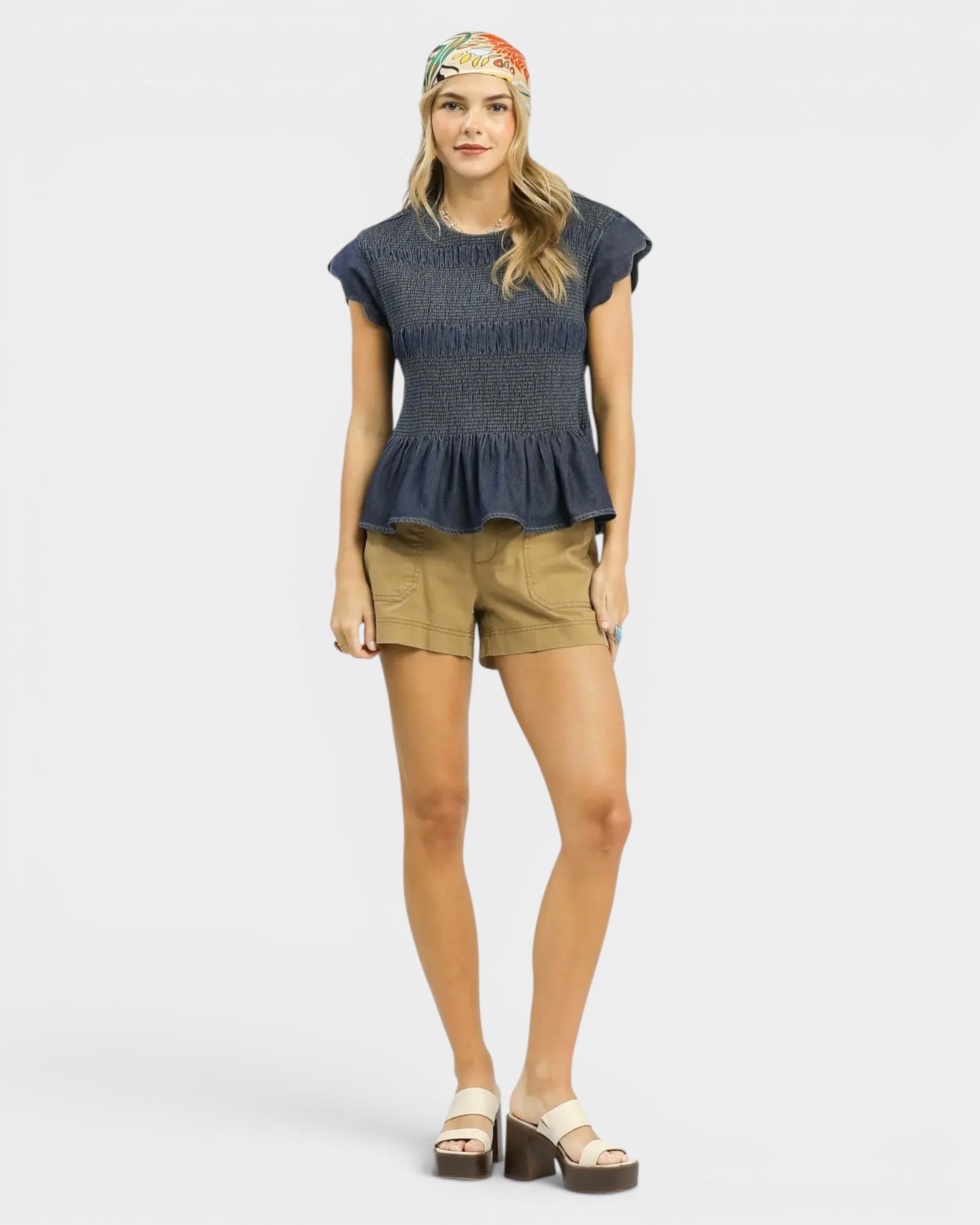 Woman wearing a dark blue peplum top and beige shorts on a white background