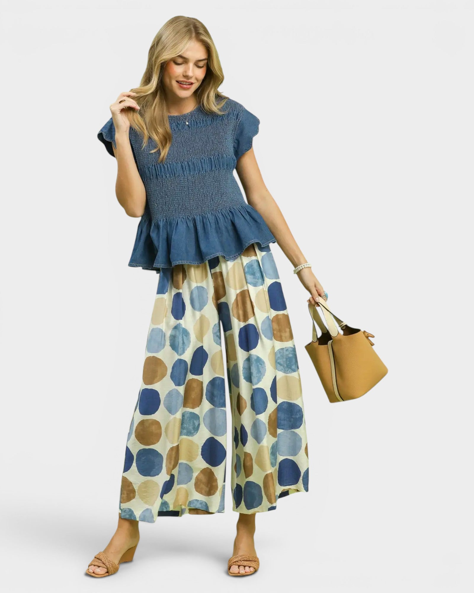 Woman wearing a blue top and patterned pants holding a brown handbag on a white background