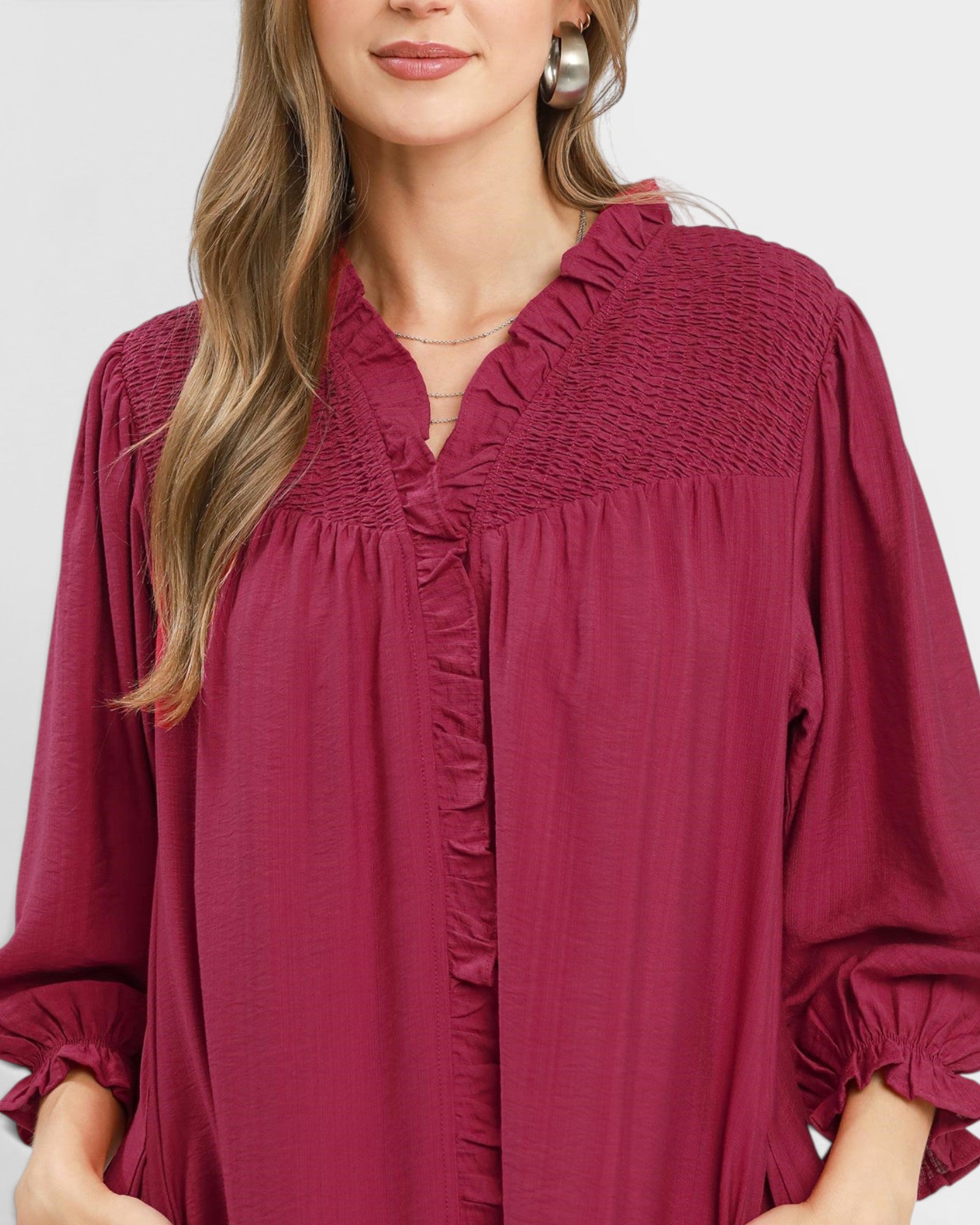 Woman wearing a burgundy dress with smocked neckline and long sleeves on a white background