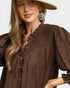 Woman wearing a brown blouse with puffed sleeves and a beige hat on a plain background