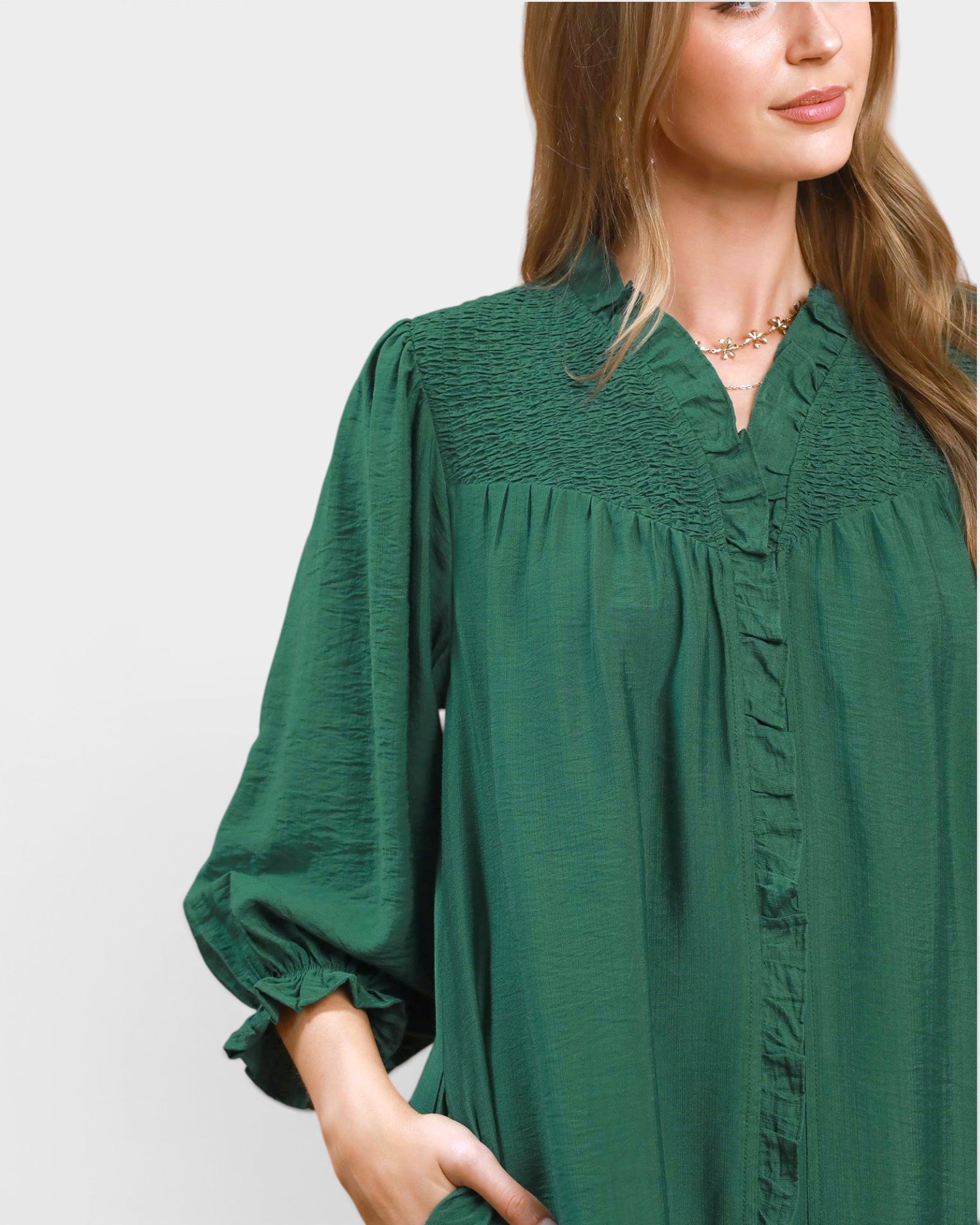 Woman wearing a green blouse with smocked details on a light gray background