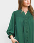 Woman wearing a green blouse with smocked details on a light gray background